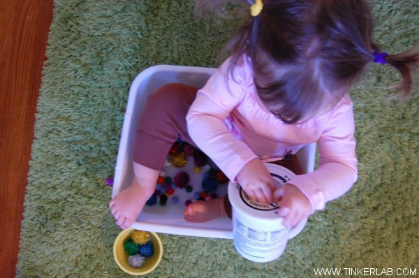 toddler sitting in plastic container with pom poms